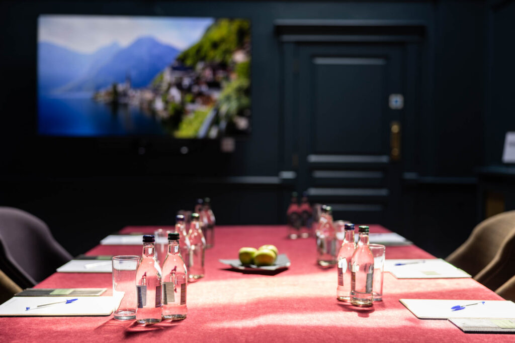 Close up of a meeting room table with still water, notepads and fruit in front of a screen