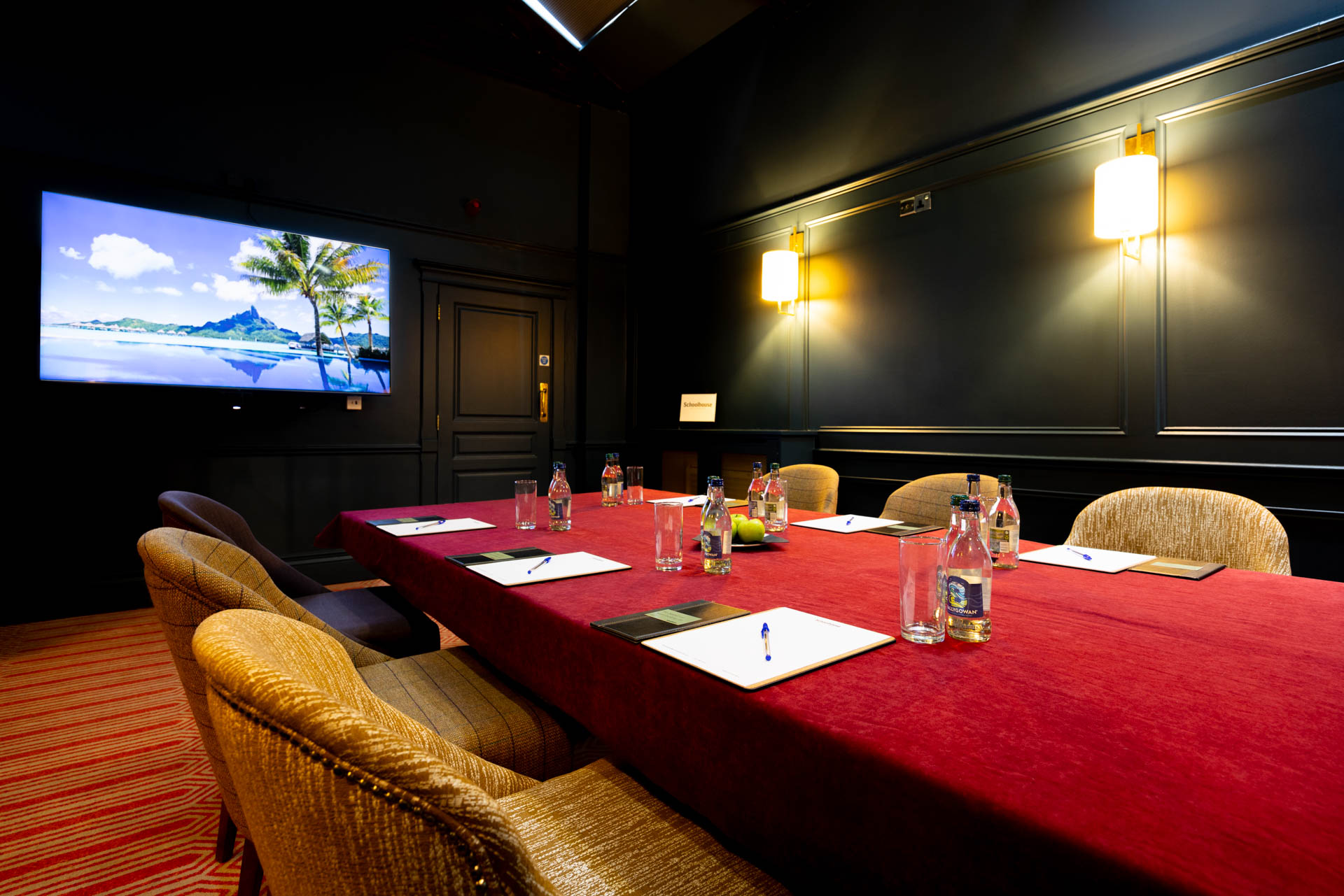 Boardroom table set for a meeting with a wall mounted screen and panelled walls at Schoolhouse Hotel