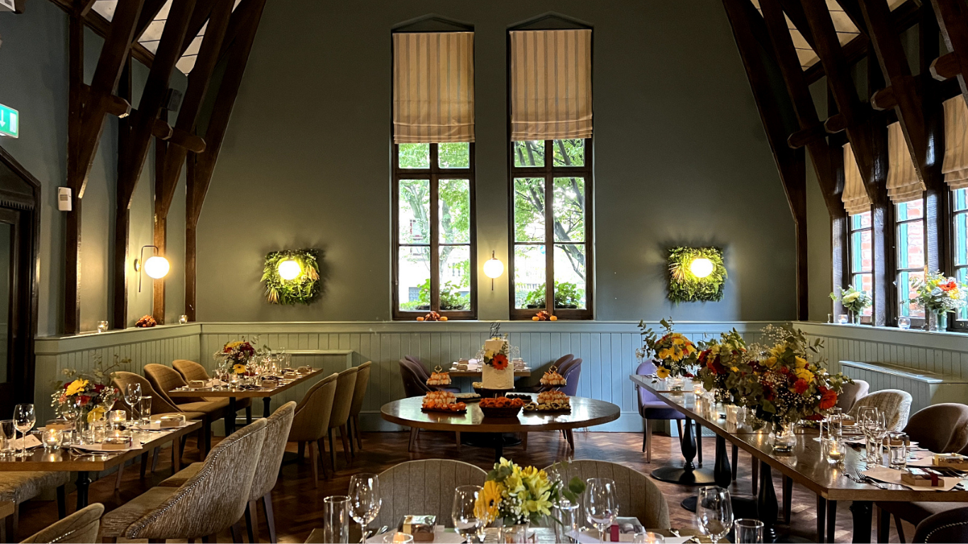 Events room set with long tables, sunflowers and a cake table beneath a vaulted beamed ceiling