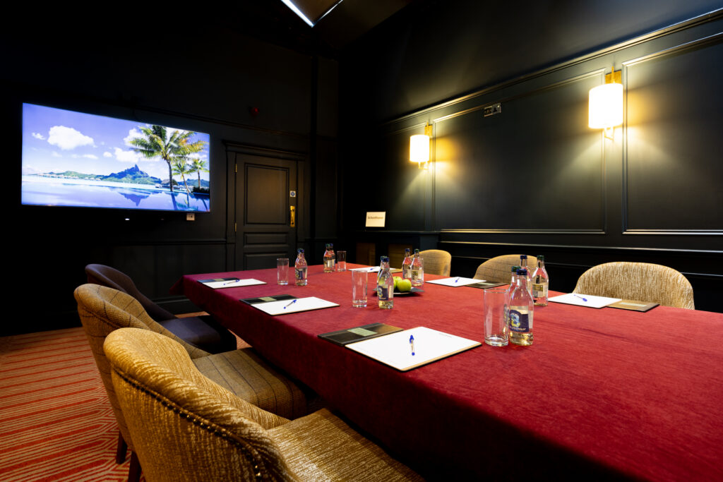 Boardroom table set for a meeting with a wall mounted screen at Schoolhouse Hotel