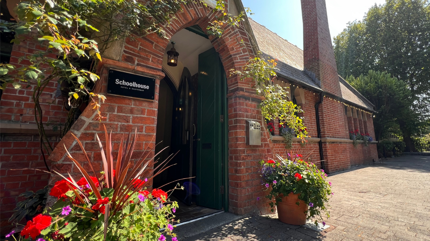 Red brick entrance to Schoolhouse Hotel and Gastrobar with a green door and flower planters