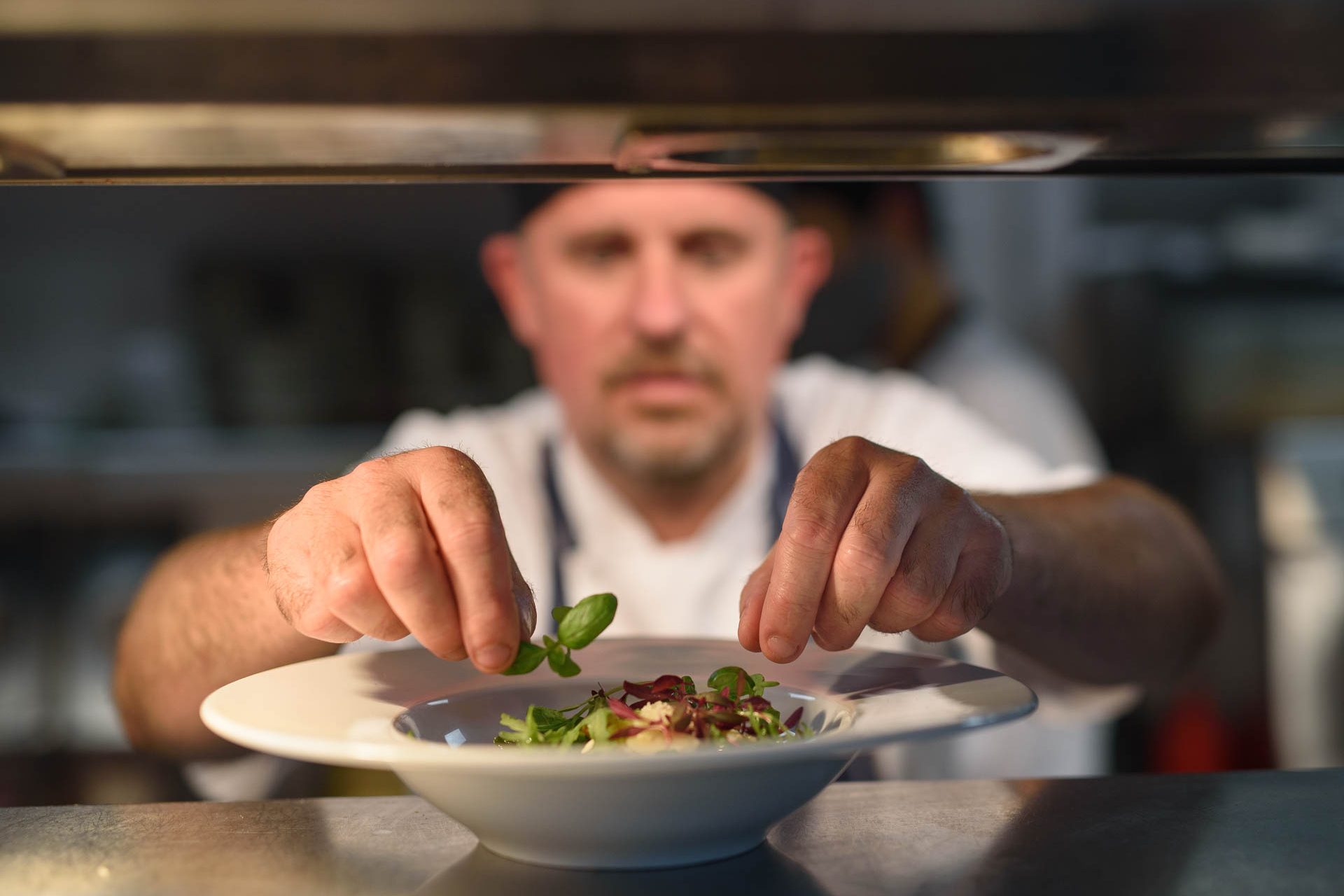 Chef plating a dish with fresh herbs at the pass in the kitchen at Schoolhouse Hotel