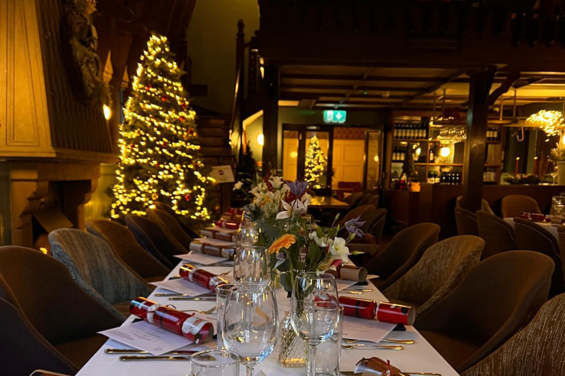 Table dressed with white linen, crackers and flowers in front of a lit Christmas tree at Schoolhouse Hotel